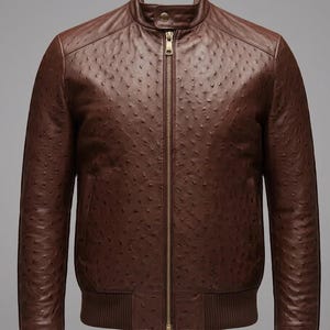 Può includere: Una giacca in pelle marrone scuro con una trama testurizzata effetto struzzo, una cerniera centrale in metallo dorato, un colletto alla coreana con un singolo bottone a pressione e bordi in maglia a coste sull'orlo per una vestibilità strutturata.