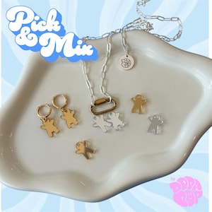 May include: A silver chain necklace with a gold-toned carabiner clasp, a round tag with a logo, and several gingerbread man-shaped charms in gold and silver tones. Two gold-toned hoop earrings with gingerbread charms are included. Text reads Pick & Mix.