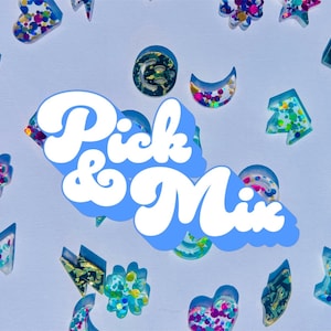 May include: A collection of small, colorful resin shapes in various forms including hearts, stars, moons, and flowers, scattered across a light background. The text Pick & Mix is displayed in large, white, bold letters with a blue drop shadow.