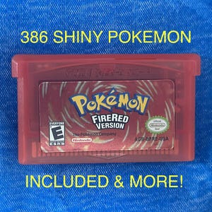 May include: A red Game Boy Advance video game cartridge for Pokémon FireRed Version. The label features the Pokémon logo, the text "FIRERED VERSION", an ESRB E rating, and the Nintendo seal. Text above and below reads "386 SHINY POKEMON INCLUDED & MORE!"