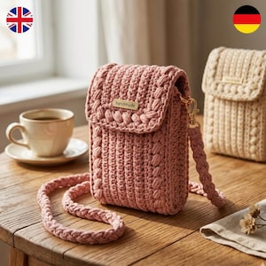 Peut inclure: Un sac bandoulière en crochet rose poudré avec un motif de points verticaux texturés, un rabat avec une étiquette métallique dorée portant l'inscription handmade et une bandoulière tressée épaisse. Un second sac beige est visible en arrière-plan.