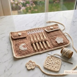 May include: A beige crochet organiser roll featuring five wooden crochet hooks, two small pockets with button closures, and decorative white moon and star appliques. Includes a matching square granny square, a flower motif, and a spool of yarn.