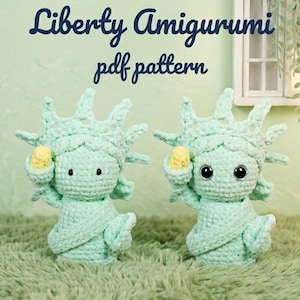 Puede incluir: Dos figuras amigurumi de ganchillo de la Estatua de la Libertad, en verde claro con detalles amarillos. Las figuras tienen grandes ojos negros y sostienen una antorcha amarilla. El texto "Liberty Amigurumi pdf pattern" está en la parte superior.