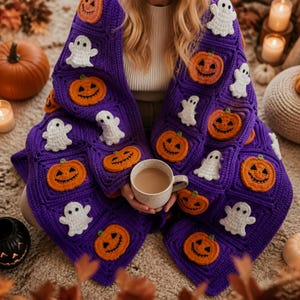 May include: A purple crochet blanket featuring a repeating pattern of orange jack-o'-lanterns and white ghosts. The blanket is constructed from square panels and is draped over a person holding a light-colored ceramic mug filled with a beverage.