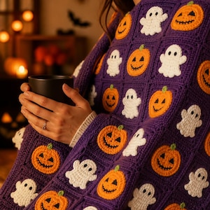 May include: A purple crochet blanket featuring a repeating pattern of white ghost appliqu&eacute;s and orange jack-o'-lantern pumpkin appliqu&eacute;s. The blanket is constructed from square motifs joined together, creating a textured, handmade textile design.