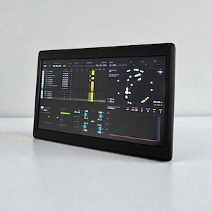 May include: A black rectangular device with a screen displaying data and graphics. The screen shows various charts, graphs, and numerical data, with a focus on performance metrics. The device is angled slightly, showcasing its sleek design and the detailed information on the screen.