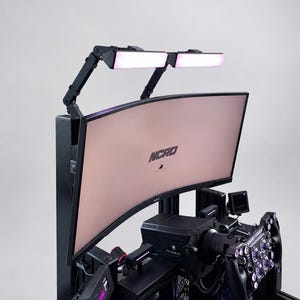 May include: A black racing simulator cockpit featuring a curved monitor with the text NCRO displayed on the screen. The setup includes a steering wheel with multiple buttons, two adjustable LED light bars mounted above the monitor, and a small display.
