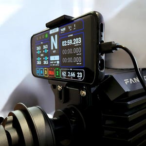 Könnte beinhalten: Ein schwarzes Smartphone, das auf einer Rennsimulator-Basis montiert ist und ein digitales Armaturenbrett mit Telemetriedaten wie Rundenzeiten, Kraftstoffständen und Ganganzeigen anzeigt. Ein schwarzes Ladekabel ist seitlich eingesteckt.
