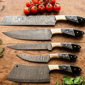 Puede incluir: Un juego de cinco cuchillos de cocina con hojas de acero damasco, virolas de latón y mangos oscuros texturizados. La colección incluye un cuchillo de pan dentado, un cuchillo de chef, un cuchillo multiusos, un cuchillo de pelar y un cuchillo carnicero.