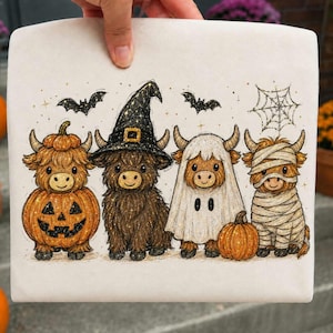 Op de afbeelding: Een wit stoffen oppervlak met een grafische illustratie van vier Highland-koeien verkleed voor Halloween. Eén koe zit in een pompoen, één draagt een heksenhoed, één is een spook en één is een mummie. Vleermuizen en een spinnenweb zijn ook afgebeeld.