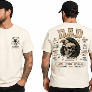 May include: A cream-colored t-shirt featuring a small front graphic of a piston and wrench with the text RAD DAD SOCIETY. The back displays a large graphic of an eagle and skull with the text DAD and various phrases including BUILT DIFFERENT.