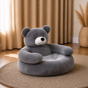 May include: A gray plush bear-shaped chair with a round seat and armrests. The bear has a white face, black nose, and small brown eyes. The chair is designed for children and is placed on a round, textured rug.
