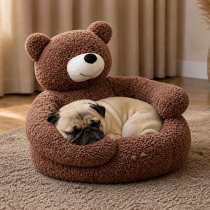 May include: A brown teddy bear dog bed with a sleeping pug inside. The bed is made of soft, plush material and has a bear-shaped head and arms. The pug is light brown with a black muzzle and ears, curled up in the bed.