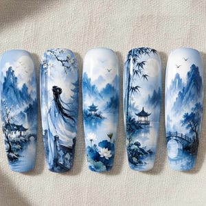 Op de afbeelding: Vijf lange, ovale kunstnagels met een blauw en wit landschapsontwerp. Elke nagel toont een andere scène van bergen, water en traditionele Chinese architectuur. De ontwerpen zijn gedetailleerd en artistiek.