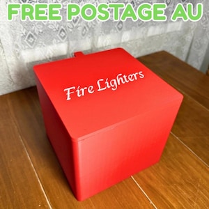 May include: A bright red square storage box with a flat lid. The top surface of the box features the white text "Fire Lighters" printed in a script font. The container has a smooth, solid-coloured finish and a simple, boxy geometric shape.