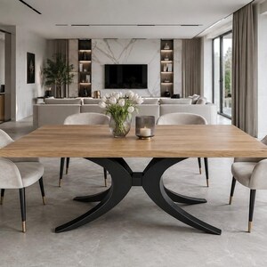 Puede incluir: Una mesa de comedor rectangular con tablero de madera de roble claro y base de metal negro con patas curvas. Cuatro sillas tapizadas en color beige claro con patas negras y puntas doradas rodean la mesa, que sostiene un jarrón de cristal con tulipanes blancos.