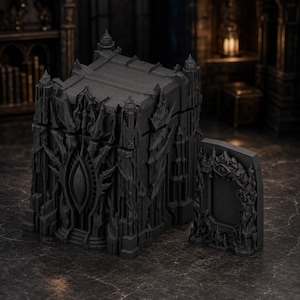 May include: A dark gray, rectangular storage box featuring intricate, jagged architectural carvings and a central eye motif on the front panel. A matching, separate rectangular lid or panel with a similar eye design sits beside the main structure.