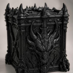 Könnte beinhalten: Eine schwarze Truhe im gotischen Stil mit aufwendigen Drachen- und Spitzendetails. Die Truhe zeigt einen Drachenkopf auf der Vorderseite und ist mit kunstvollen Schnitzereien und spitzen Akzenten verziert, wodurch eine Fantasy-Ästhetik entsteht. Die Truhe hat eine einfarbige, dunkle Farbe.