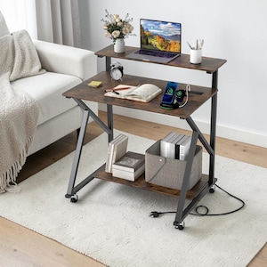 May include: A multi-tiered rolling desk with a dark wood grain finish and a black metal frame. The desk features a top shelf for a laptop, a middle workspace with a charging station, and a bottom storage shelf. It includes four caster wheels.