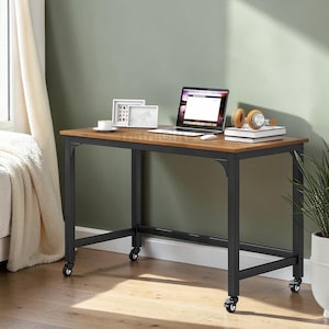 May include: A rectangular desk with a brown wood-grain top and a black metal frame featuring four caster wheels. On the desk sits an open laptop, a white mug, two small framed pictures, a stack of books, and a pair of tan over-ear headphones.