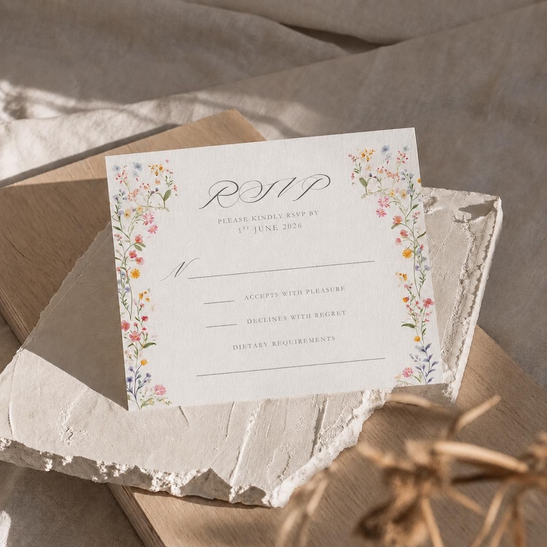 Close-up of an editable wildflower wedding RSVP card printed on textured white cardstock, styled on neutral linen and stone with warm natural sunlight.