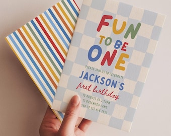 May include: A first birthday invitation card with a light blue and white checkered pattern and the text "FUN TO BE ONE" in colorful letters, paired with a matching envelope featuring vertical stripes in red, blue, yellow, and green.