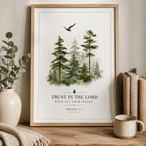 Puede incluir: Una lámina de arte mural enmarcada que presenta una escena de bosque en acuarela con pinos verdes y un pájaro en vuelo. Debajo de los árboles, el texto dice: TRUST IN THE LORD WITH ALL YOUR HEART. PROVERBS 3:5. La impresión tiene un marco de madera clara.