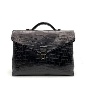 Puede incluir: Maletín negro con un patrón texturizado similar al de un cocodrilo. El bolso tiene un asa superior y un cierre de metal. Las palabras "Original Reptile Bags" están impresas en el bolso.