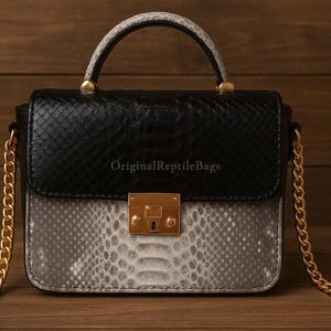 Op de afbeelding: Een kleine, zwart-grijze handtas met slangenpatroon, een gouden kettingriem en een handvat aan de bovenkant. De tas heeft een gouden sluiting en de tekst "OriginalReptileBags" is afgedrukt.