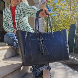 Puede incluir: Un bolso tote grande, azul oscuro con un patrón texturizado similar al de un reptil. El bolso tiene dos asas y una borla decorativa. El texto "Original Reptile Bags" es visible en el bolso.