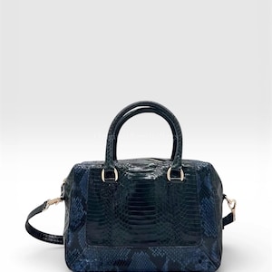 May include: A dark teal handbag with a snakeskin pattern. The bag has two top handles and a detachable shoulder strap. Gold-coloured hardware accents the bag, including the zip and strap attachments. The bag is rectangular with a structured shape.