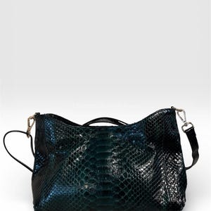 Peut inclure: Un sac à main vert foncé avec un motif peau de serpent. Le sac a une poignée supérieure et une bandoulière amovible. La quincaillerie est de couleur argentée. Le sac est fait d'un matériau brillant et texturé.