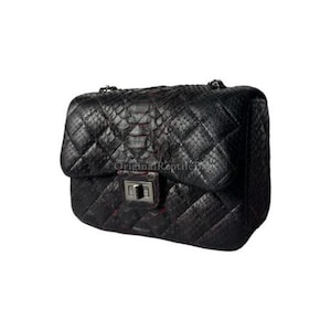 Könnte beinhalten: Schwarze, gesteppte Lederhandtasche mit silberner Kette und Schnallenverschluss. Die Tasche hat ein Rautenmuster und einen Klappenverschluss. Der Text "Original Reptile" ist sichtbar.