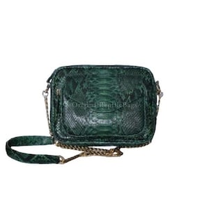 Könnte beinhalten: Dunkelgrüne, rechteckige Umhängetasche mit Schlangenmuster. Die Tasche hat einen langen, verstellbaren Riemen und ein goldfarbenes Kettendetail. Der Text "Original Reptile Bags" ist auf der Tasche zu sehen.