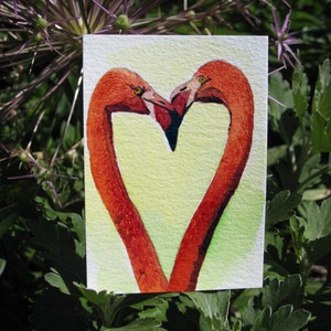 May include: Watercolor painting of two pink flamingos with their necks intertwined to form a heart shape. The background is a light yellow with green accents.