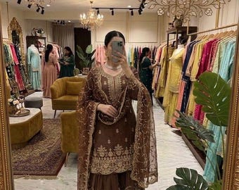 Puede incluir: Un conjunto marrón de tres piezas que consta de una túnica de manga larga, pantalones anchos y una dupatta transparente a juego. El conjunto presenta un intrincado bordado dorado en el escote, el dobladillo y la tela, con un borde festoneado.