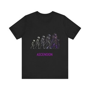 Peut inclure: Un t-shirt noir à manches courtes avec une impression graphique montrant une progression évolutive de créatures extraterrestres, allant d'un petit être à une grande silhouette en armure vêtue d'une robe violette. Le mot ASCENSION est imprimé en dessous.