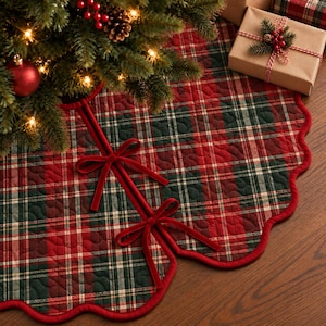 May include: A round quilted Christmas tree skirt featuring a red, dark green, and white plaid pattern with a scalloped edge trimmed in red. The skirt includes two red velvet ribbon ties for closure and a quilted texture throughout the fabric.