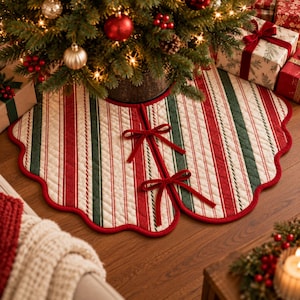 May include: A round quilted Christmas tree skirt featuring vertical stripes in red, dark green, and cream. The fabric has a diamond-stitched texture with a scalloped red edge. Two red fabric ties secure the opening at the front of the skirt.