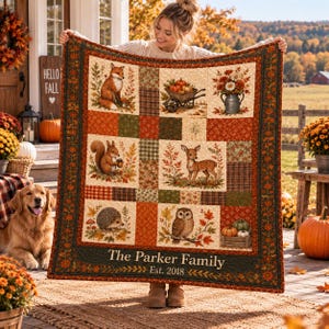 Pode incluir: Uma colcha retangular com design de patchwork apresentando ilustrações de uma raposa, um esquilo, um cervo, um ouriço, uma coruja, abóboras e flores. A borda inferior exibe o texto The Parker Family Est. 2018 em uma moldura verde-escura.