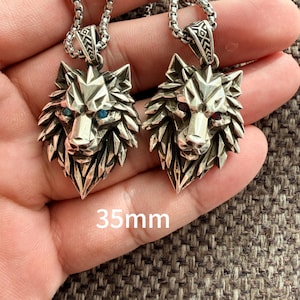 May include: Two silver-toned wolf head pendants on link chains, each measuring 35mm. One wolf features blue eyes, while the other features red eyes. The pendants have a faceted, geometric design with detailed metalwork on the bails.