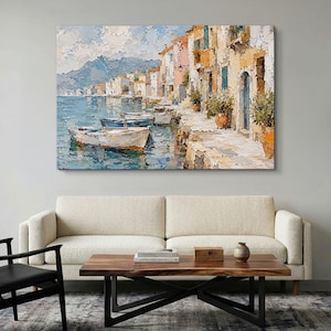 May include: An oil painting on canvas depicting a coastal village scene with textured brushstrokes. Several small boats float on blue water near a stone quay lined with multi-colored buildings, potted plants, and distant mountains under a cloudy sky.