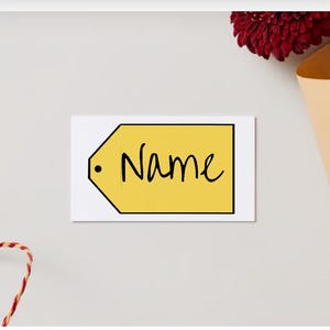 May include: A white card with a yellow tag that says "Name" in black cursive writing. The tag has a black circle in the upper left corner.