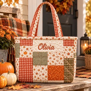 May include: A quilted tote bag featuring a patchwork design of red and white gingham, green and white gingham, and floral patterns in orange and cream. The bag has two matching handles and the name Olivia embroidered in orange on the front.