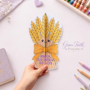 Op de afbeelding: Een papieren knutselwerk in de vorm van een korenschoof met een gele strik, voorzien van een lachend gezicht en de tekst "JESUS, THE BREAD OF LIFE" in paarse letters. Het ontwerp is ingekleurd in geel- en bruintinten als religieuze knutselactiviteit.