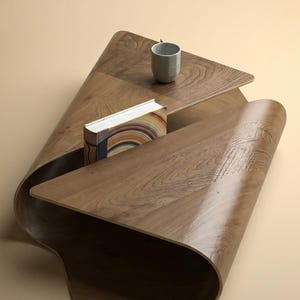 Puede incluir: Una mesa de centro moderna y escultural de madera con un diseño único y fluido. La mesa cuenta con un estante incorporado que sostiene un libro con páginas coloridas y una pequeña taza gris. La madera tiene una veta cálida y natural.