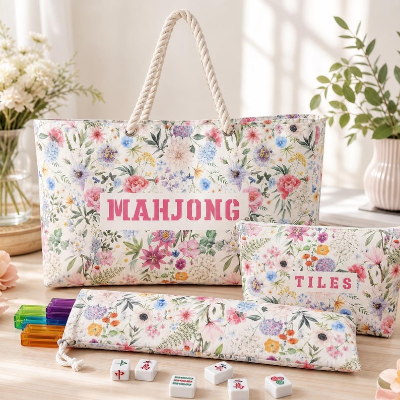 May include: A floral print tote bag with rope handles featuring the text MAHJONG, a matching zippered pouch labeled TILES, and a long rectangular case containing colorful translucent tiles, with several individual mahjong tiles scattered nearby.