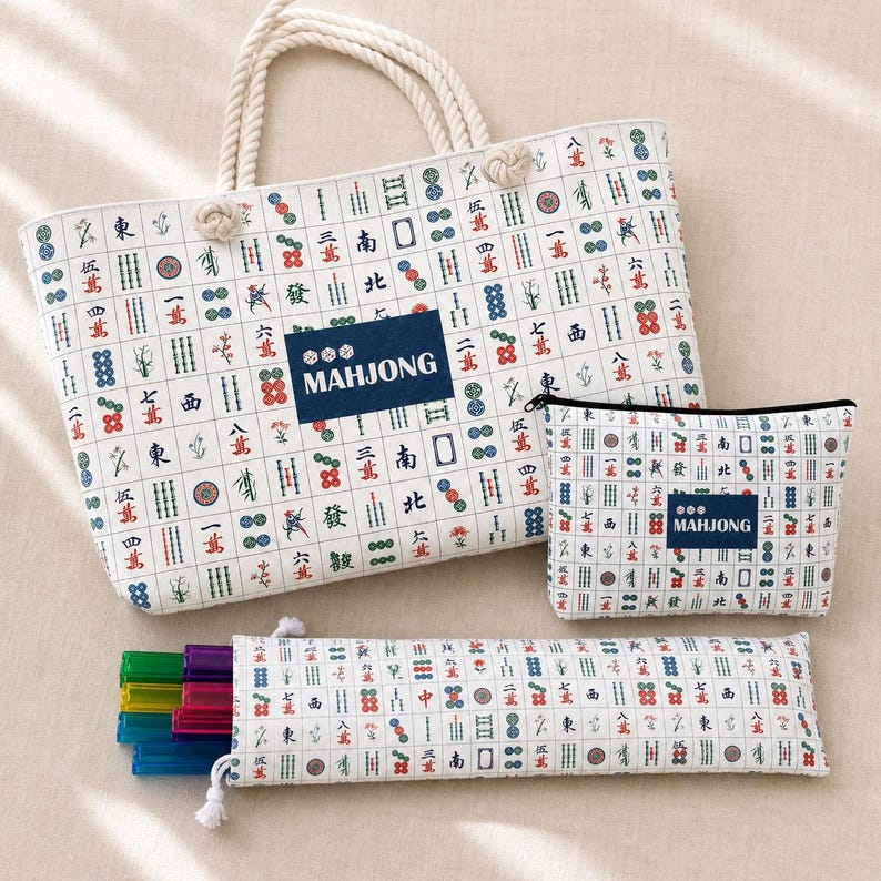 May include: A white tote bag, a rectangular zippered pouch, and a long narrow case, all featuring a repeating pattern of colorful mahjong tile symbols. Each item has a dark blue rectangular patch with the white text MAHJONG printed on it.