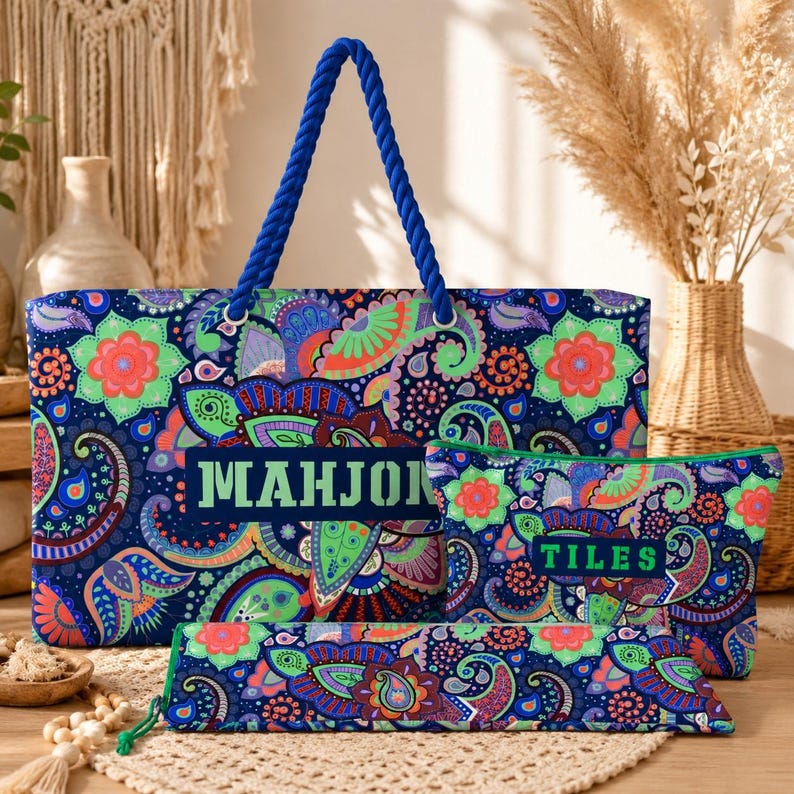 May include: A large rectangular tote bag, a smaller zippered pouch, and a long slim case, all featuring a vibrant blue, green, orange, and purple paisley pattern. The tote has blue rope handles and the text MAHJONG. The pouch features the text TILES.
