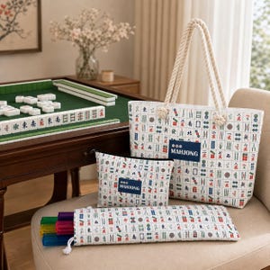 May include: A white tote bag, a matching zippered pouch, and a long rectangular case, all featuring a repeating pattern of colorful mahjong tiles. The tote bag has thick, cream-colored rope handles and a dark blue label with the text MAHJONG.